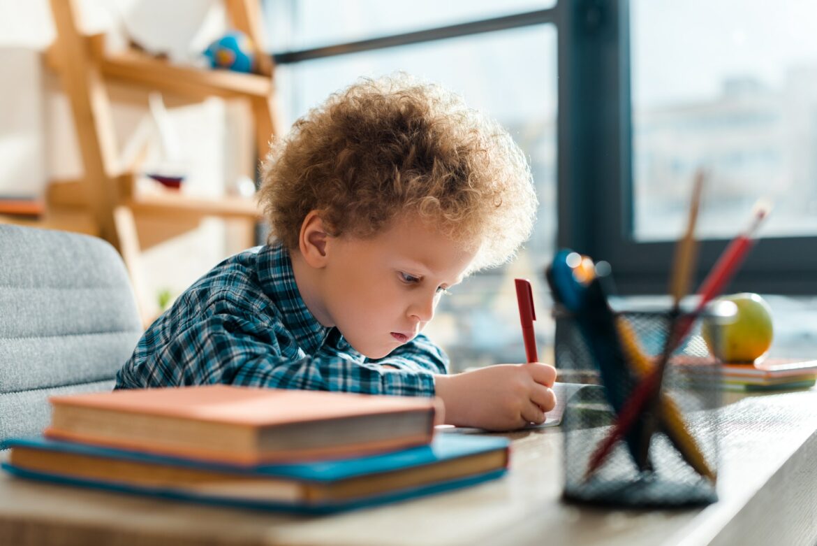 selective-focus-of-curly-kid-writing-near-books.jpg