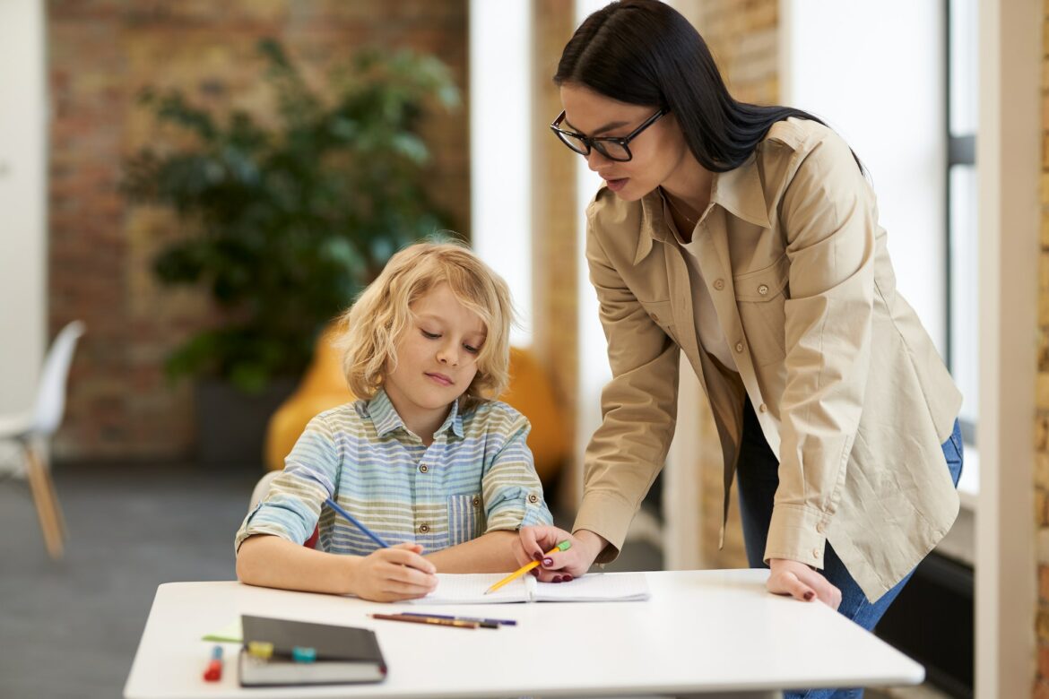 supportive-young-female-teacher-in-glasses-helping-little-boy-with-the-task-kid-studying-in.jpg
